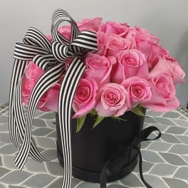 Pink roses in a black hatbox with a black-and-white striped ribbon