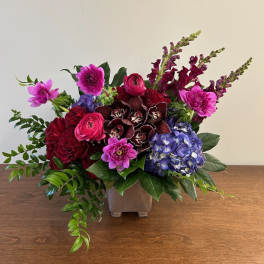 Mixed bouquet in a square vase with pink, red, purple, and blue flowers
