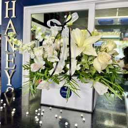 White floral arrangement in a gift box with ribbon and a handle