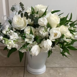 White floral arrangement in a white pedestal vase with green foliage