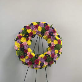 Circular floral wreath on a black stand with pink, yellow, and purple flowers