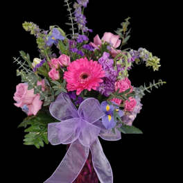 Pink and purple mixed bouquet in a glass vase with a lavender bow