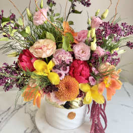 Colorful arrangement of pink, yellow, orange and purple flowers in a white ceramic pot on marble.