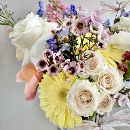 Mixed bouquet of roses, daisies, and pink blossoms in a glass vase with ribbon