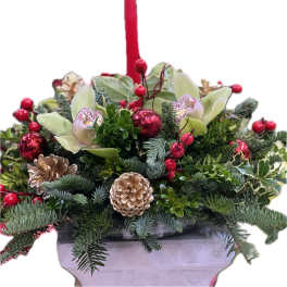 Holiday floral arrangement with red berries, orchids, and pinecones in a container