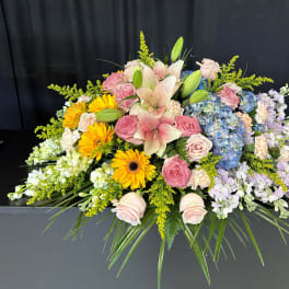 Large floral casket spray with pink roses, lilies, hydrangeas, and yellow daisies