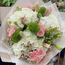 Bouquet of pink roses, white hydrangeas, and green pom-pom flowers wrapped in pale paper.
