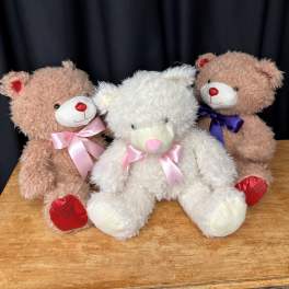 Three teddy bears with satin bows sitting on a wooden surface