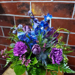 Purple and blue floral arrangement in a square vase