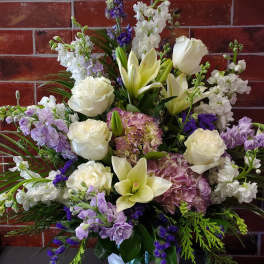 White roses, lilies, and purple flowers in a white urn vase