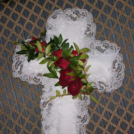 Red roses and greenery arranged on a white lace cross