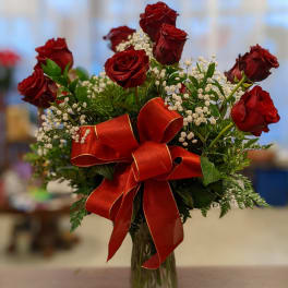 Red roses in a glass vase with baby's breath and a large red ribbon