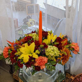 Colorful floral arrangement in a clear glass bowl with a tall orange candle