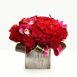 Red rose arrangement with pink orchids in a square vase