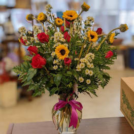 Bouquet of red roses and yellow flowers in a clear glass vase with a pink ribbon