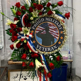 Standing wreath with red roses, white lilies, and a veteran tribute sign