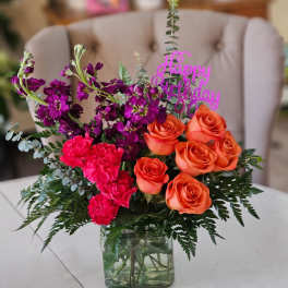 Orange roses and pink flowers in a glass vase with a birthday topper