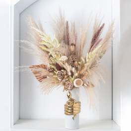 Dried pampas grass and neutral preserved blooms in a white vase wrapped with a gold snake accent