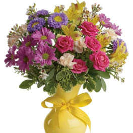 Colorful bouquet of daisies, roses, and alstroemeria in a yellow vase with a ribbon