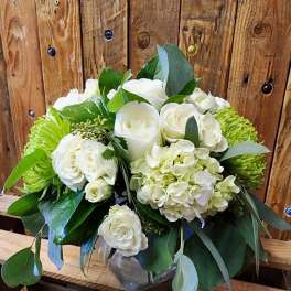 White roses and hydrangeas in a glass vase with green foliage