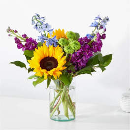 Sunflowers and purple-blue flowers in a clear glass vase