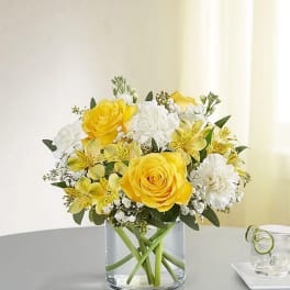 Yellow roses and white flowers in a clear glass vase