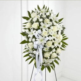 White floral standing spray on an easel with a ribbon bow