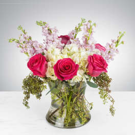 Low vase of hot pink roses, white hydrangeas, lavender stock and trailing greenery.
