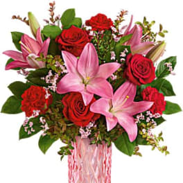 Pink lilies and red roses arranged in a pink glass vase