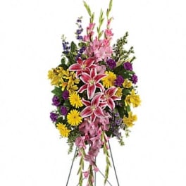 Standing floral spray with pink lilies, yellow daisies, and purple flowers on an easel