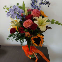 Mixed bouquet with sunflowers, roses, lilies, and blue flowers in a glass vase