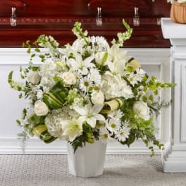 White floral arrangement in a white vase with lilies, roses, and daisies