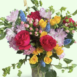 Mixed bouquet of roses, lavender blooms, and blue grape hyacinth in a glass vase