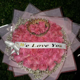 Round bouquet of pink roses with baby’s breath, crown accent, and a ‘We Love You’ banner.