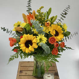 Bouquet of sunflowers, orange roses, and lilies in a glass vase