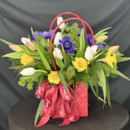 Mixed bouquet in a red handled gift bag with a red ribbon