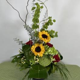 Tall floral arrangement with sunflowers and red roses in a black vase