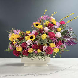 Mixed bouquet of pink, yellow, and red flowers in a white vase