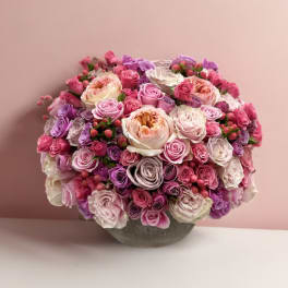 Round bouquet of pink, lavender, and white roses in a gray vase