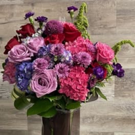 Mixed bouquet of pink, red, purple, and blue flowers in a tall clear vase
