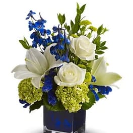White lilies and roses with blue flowers in a square glass vase