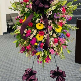 Large standing floral spray with mixed bright blooms and purple ribbons