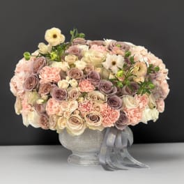 Large pastel bouquet of roses and carnations in a gray vase with ribbon