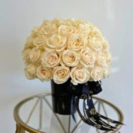 Cream rose bouquet in a black vase with dark ribbon