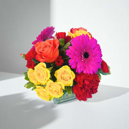 Bright mixed bouquet of roses, gerbera daisies, and carnations in a glass vase