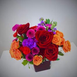 Bouquet of red and orange roses with purple and pink flowers in a dark vase