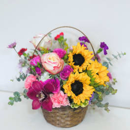 Colorful basket arrangement with sunflowers, roses, carnations, and an orchid in a woven basket