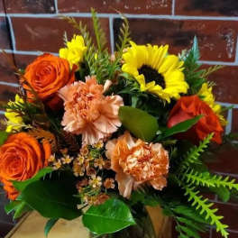 Bouquet of orange roses, yellow sunflowers, and peach carnations in a glass vase