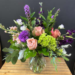 Mixed bouquet of pink, purple, and green flowers in a clear glass vase