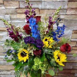 Mixed bouquet with sunflowers, roses, and blue flowers in a glass vase